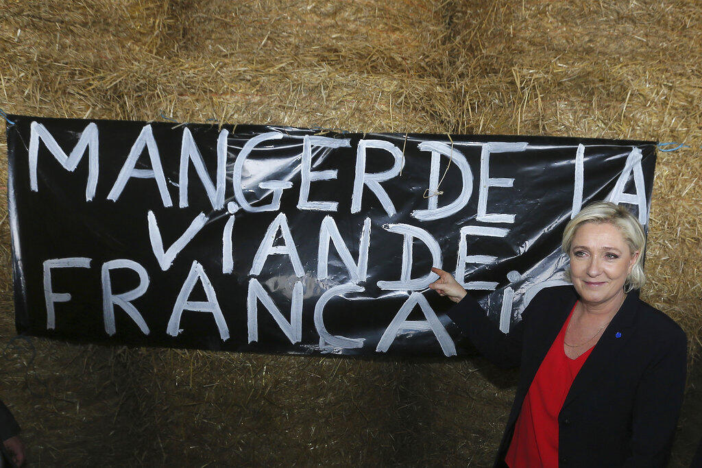 Líder da extrema direita francesa Marine Le Pen posa ao lado de um cartaz com a frase "Comer carne francesa", durante visita a uma produção de suínos em Pordic, no oeste da França. (30 de março de 2017)