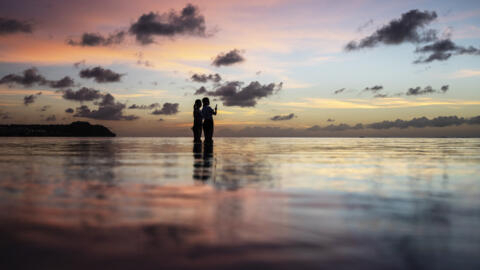 Tourists watch the sun set along a popular beach in Tamuning, Guam.