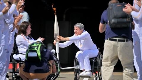 Former French wheelchair fencer Emmanuelle Assmann (C) holds the torch of the Paris 2024 Paralympic Games after arrival of the Paralympics flame at the entrance of the Channel Tunnel in Coquelles, northern France, on August 25, 2024. 