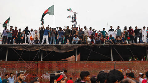 Manifestantes mostram bandeiras de Bangladesh no teto da residência da ex-primeira-ministra, em Daca, Bangladesh, após o anúncio de sua demissão, em 5 de agosto de 2024. 