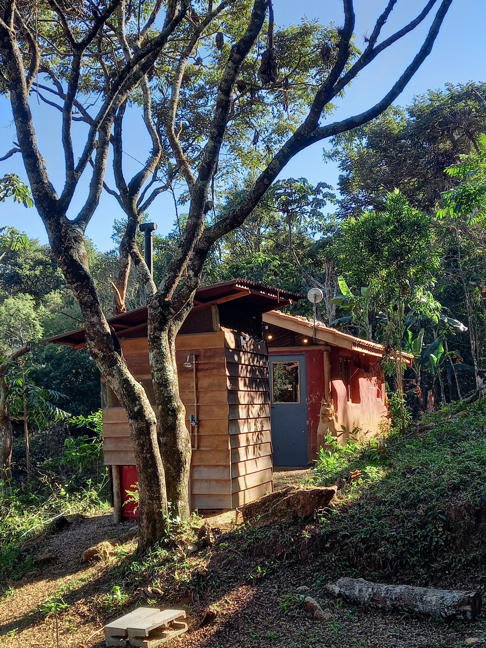 O Sítio Iandeva conta com um banheiro seco no modelo mais atualizado da SANA e uma cozinha coletiva feita em cob – uma técnica de construção com terra. Aqui é possível ver a parte de trás do banheiro seco e a porta azul se abre para a cozinha coletiva