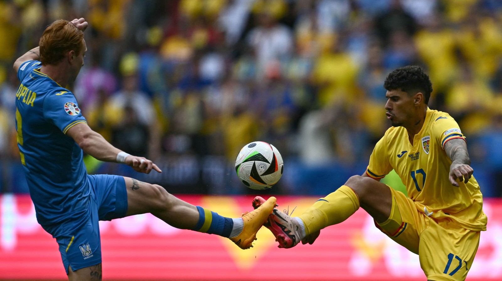 O zagueiro ucraniano nº 02 Yukhym Konoplia e o atacante romeno nº 17 Florinel Coman disputam a bola durante a partida de futebol do Grupo E da UEFA Euro 2024 entre a Romênia e a Ucrânia na Arena de Futebol de Munique — Foto: Fabrice COFFRINI / AFP