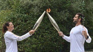 Primeiro portador da tocha, medalhista de ouro olímpico no remo em 2020, Stefanos Ntouskos acende a tocha segurada pela nadadora olímpica francesa, Laure Manaudou, ao iniciar sua corrida com a tocha olímpica após a cerimônia de acendimento da chama para os Jogos Olímpicos Paris 2024 — Foto: Valerie GACHE / AFP