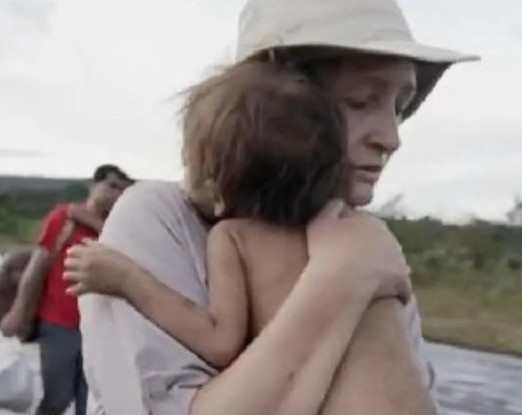 Sônia Bridi carrega uma criança Yanomami nos braços, em reportagem gravada para o Fantástico