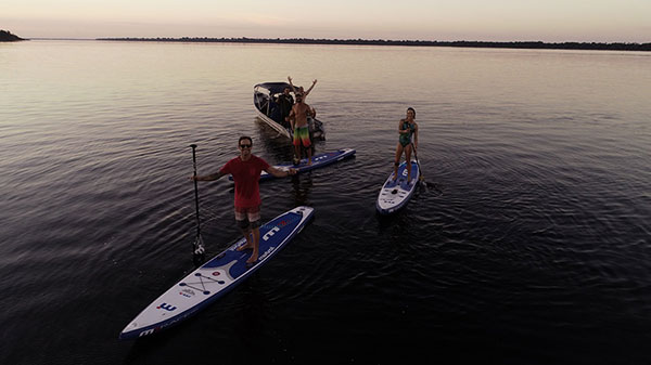 Foto de um grupo de quatro homens e uma mulher no Rio Negro. Dois dos homens estão dentro de um barco enquanto outros dois e a mulher estão posando em cima do standup paddle.