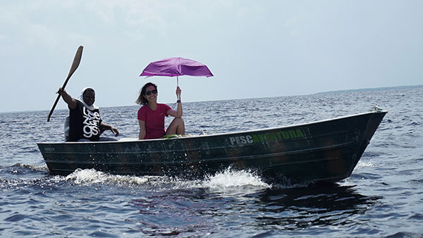 Foto de Carol Barcelos, carregando uma sombrinha aberta, navegando pelo Rio num barco de pesca.