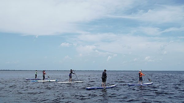 Foto do horizonte, com o Rio Negro na parte de baixo e cinco pessoas praticando standup paddle.