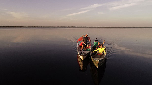 Foto do Rio Negro, ao por do sol, com cinco pessoas navegando em dois barcos de pesca.