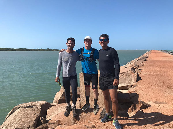 Conservani e dois homens em cima de um pedra com o mar atrás.