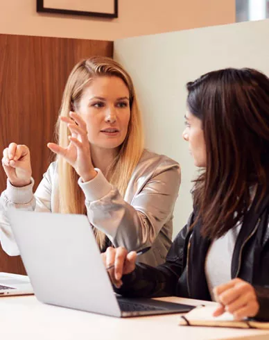 Two Young Businesswomen In Meeting Around Table In Modern Open Plan Workspace