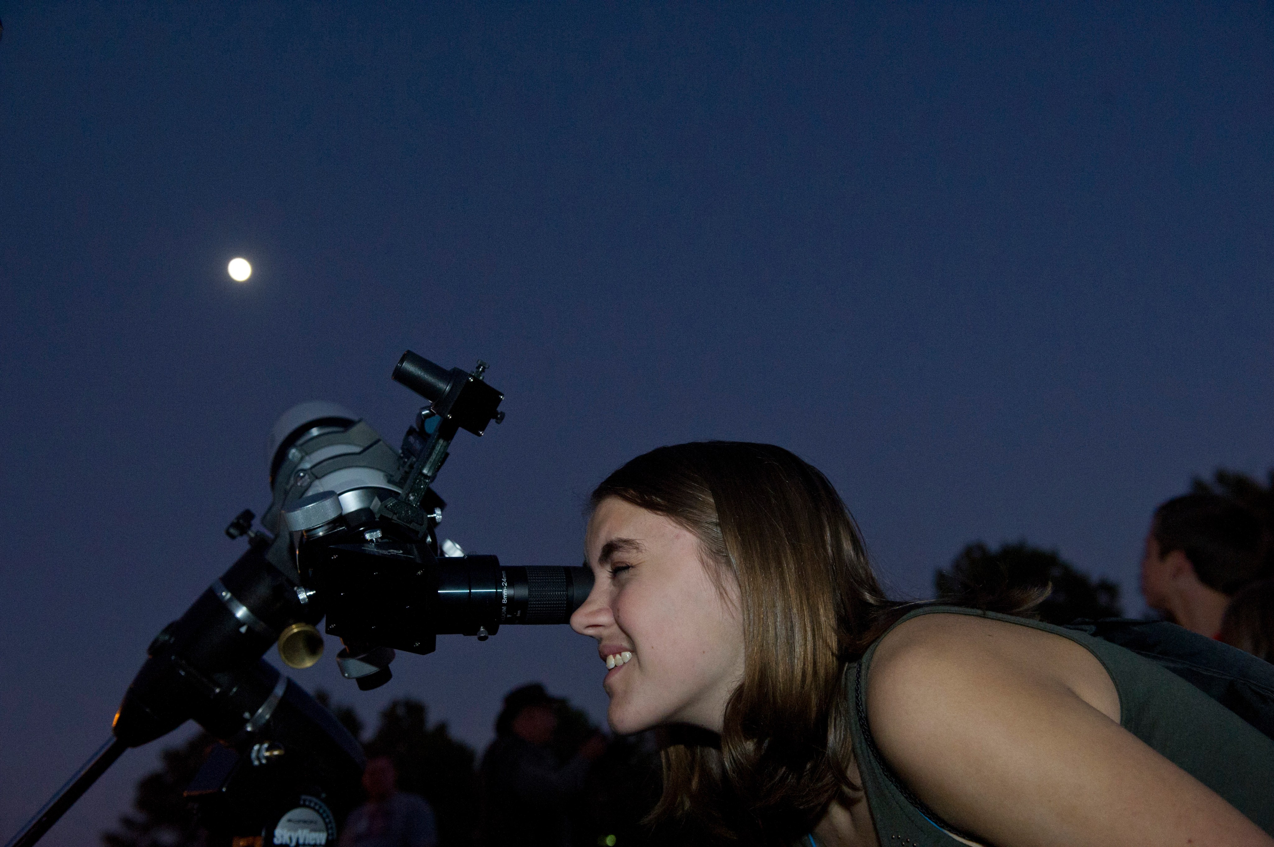 A woman peers at the Moon through a telescope.