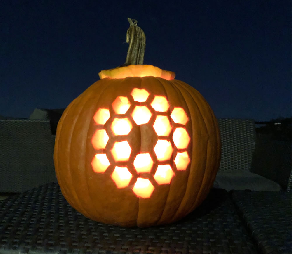 View of an illuminated jack-o'-lantern style pumpkin carved with an image of the 18 hexagon mirror segments of the James Webb Space Telescope.