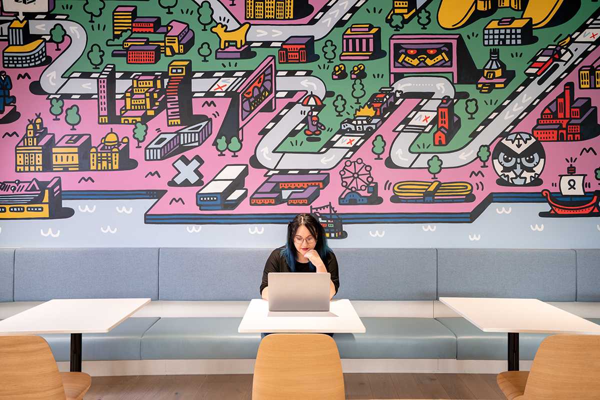 Woman sitting alone on her laptop at a large conference table - she's deep in thought looking at her screen.