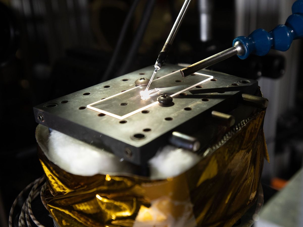 3 metal rods pointed onto a glass plate on top of a metal plate with holes in it 