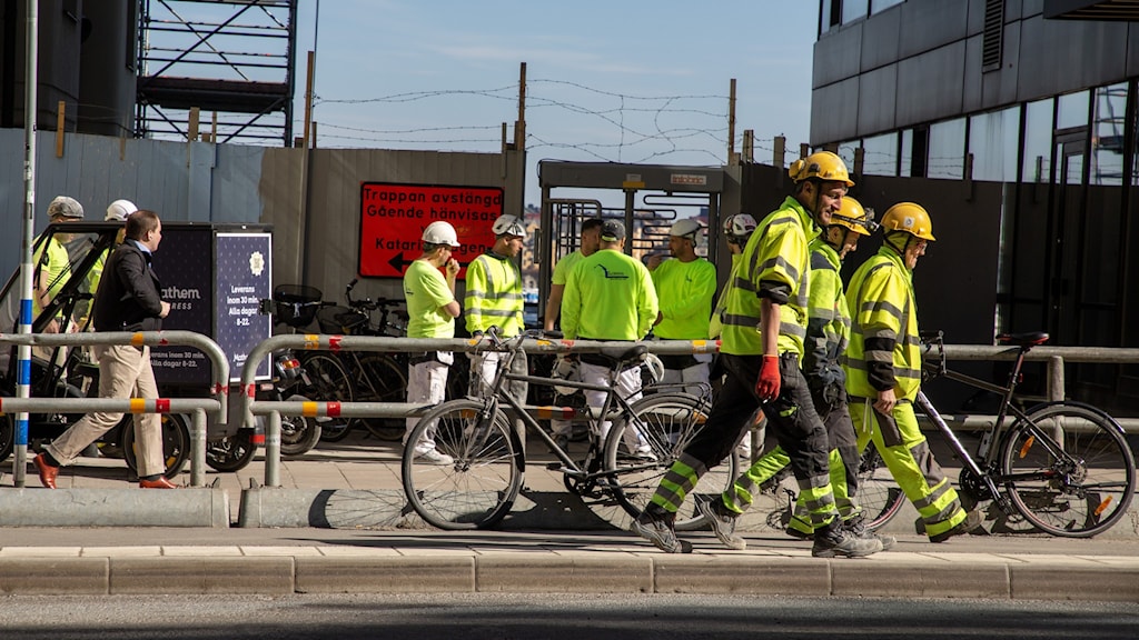 Construction workers on a site, they are wearing bright high-vis jackets and hard hats.