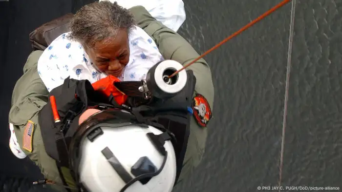 A U.S. Navy Petty Officer retrieves an evacuee of Hurricane Katrina from a rooftop onto a helicopter.