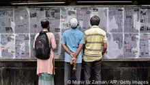 People stand in the street and read Bangladesh's local newspapers pasted along a wall in the capital Dhaka in September 2023 ahead of elections.