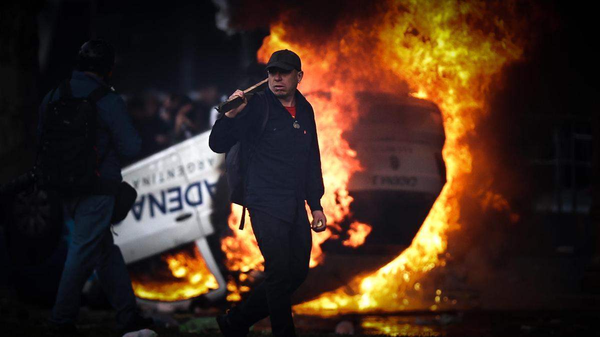 Un hombre camina frente a un auto en llamas en una protesta a las afueras del Congreso.