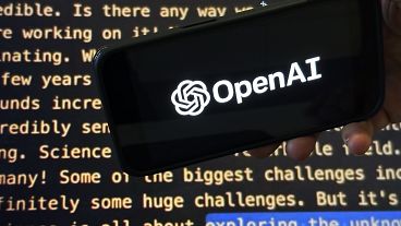 Das OpenAI-Logo erscheint auf einem Mobiltelefon vor einem Bildschirm, der einen Teil der Website des Unternehmens zeigt.