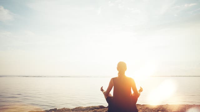 Frau meditiert bei Sonnenuntergang am Strand.