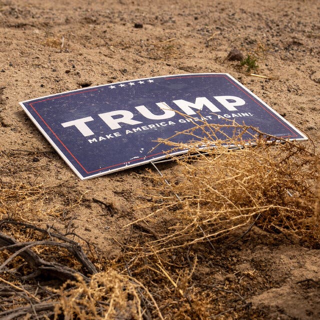 A blue Trump sign sits at the end of a dirt road.