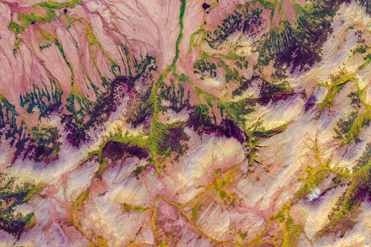 A satellite view of a mountainous landscape with colorful pink striated rock formations and patches of green vegetation.