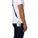 Coque Crossbody Flex Quartz de Tech21, bandoulière incluse attachée au bas de la coque contenant un iPhone, suspendue à la droite d’une personne qui porte un tee-shirt blanc et un jean