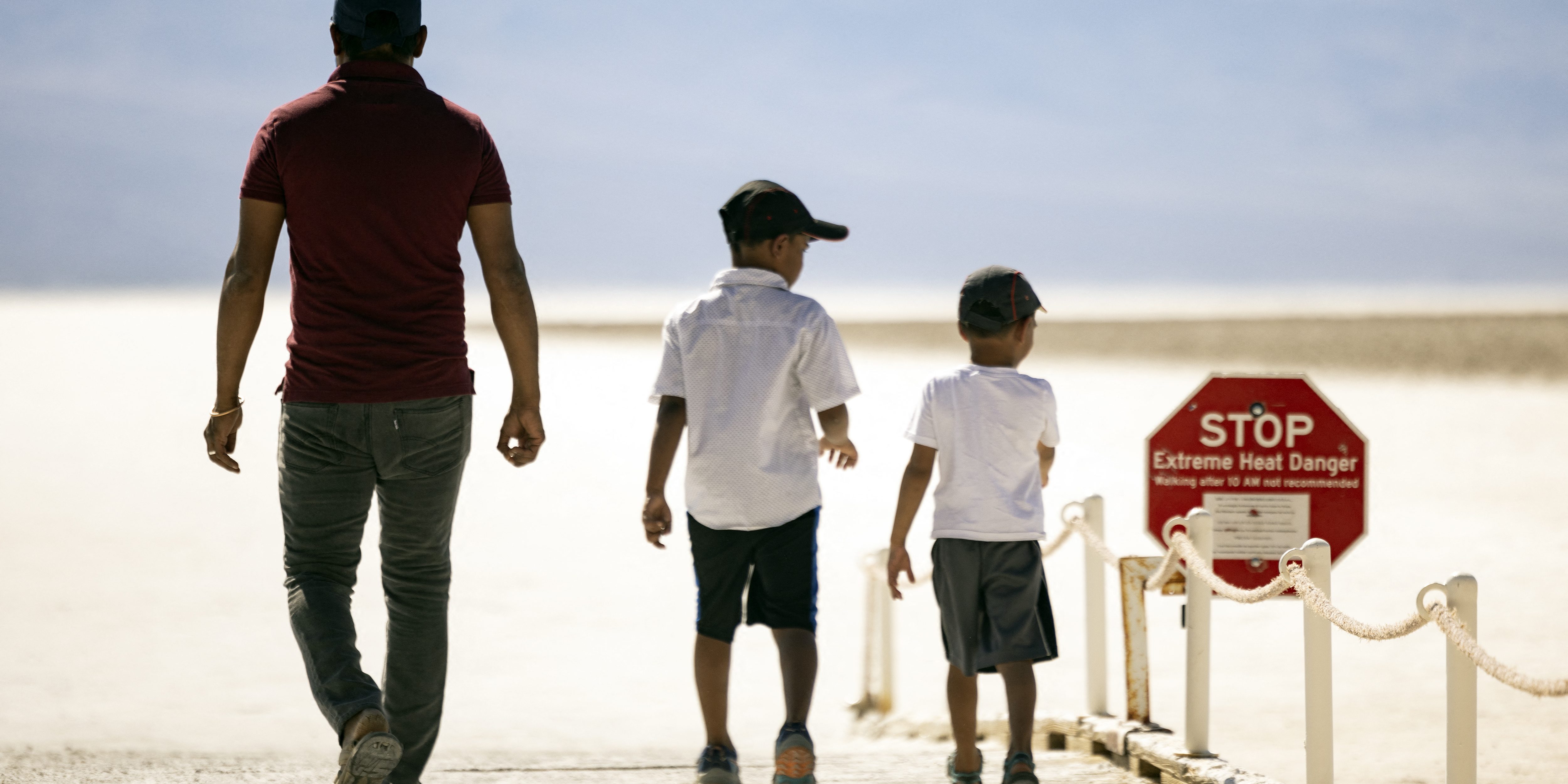 Visitors walk past a sign reading "Stop Extreme Heat Danger" at Badwater Basin in Death Valley National Park, near Furnace Creek, during a heatwave impacting Southern California on July 7, 2024. Temperatures in Death Valley could reach as high as 130 degrees Farenheit (54 degrees Celsius) on Sunday, according to US National Weather Service. (Photo by ETIENNE LAURENT / AFP) (Photo by ETIENNE LAURENT/AFP via Getty Images)