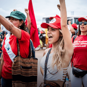 A group of people with their hands in the air rolled into fists. They are wearing red and green caps and are marching on the street