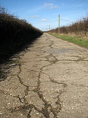 Une petite route de campagne, dont la chaussée comporte de multiples fissures.