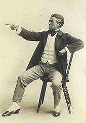 A young Claude Rains dressed as a lawyer, sitting on a chair and pointing