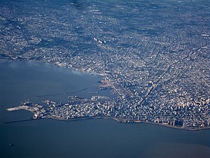 View of coastal city with higher-rise buildings and a port in the foreground and lower-rise buildings further away