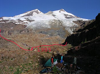 Frontale Farbfotografie eines Berges mit Schneespitze und unten rechts drei Camper mit Ausrüstung. In der Mitte und ein gutes Stück vom Schnee entfernt ist eine rote, ungerade Linie mit der Jahreszahl 1985 horizontal eingezeichnet. Unten rechts steht das Aufnahmedatum „08.12.2003“