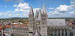 A grey stone cathedral with a central square tower flanked by 4 square towers. Surrounded by the red roofs of the old city.