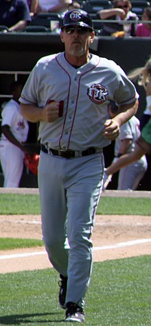 A man in a gray baseball uniform and navy blue batting helmet