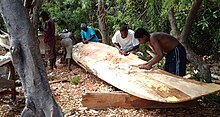 A group of men building a wooden boat in a forested area