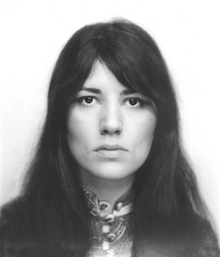 Black-and-white photograph of a woman with long dark hair holding a microphone and singing