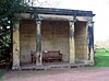 A stone loggia with four columns supporting an entablature, and containing a wooden seat