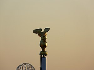 Aigle installé en haut d'un des mâts du cimetière, vu de dos.
