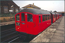 A red 1938 Bakerloo line train bound for Harrow & Wealdstone waiting at a platform at Harlesden station with its doors open