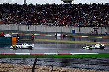 Photo de la BGP 001 de Button, suivie par celle de Barrichello sur une piste humide. Au loin, Trulli