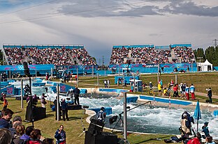 Crowds in temporary stands watch competitors in rushing water.