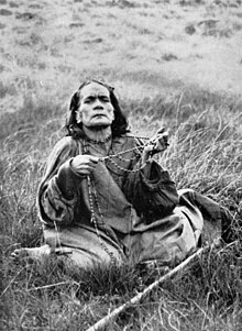 Une femme agenouillée dans l'herbe avec une chapelet tenu d'une main à l'autre, en contemplation.