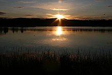 the sun half-above a mountain, with a reflection on the lake below, encompassed in nautical twilight