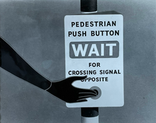 A black and white illustration showing a close-up view of a pedestrian pressing the call button at a Panda crossing