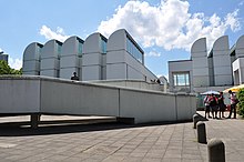 Photographie en couleur d’un musée vu en contre-plongée. Rampe d’accès monumentale au premier plan.