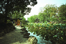 Men and women stand on curving rock formations overlooking a pond containing flowery plants.