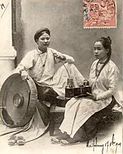 Two women wear áo ngũ thân, the form of the ao dai worn in the 19th and the early 20th centuries