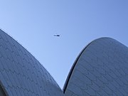 Phần trên của một công trình hình cong không thể nhận ra bên dưới bầu trời xanh, cùng với một chiếc trực thăng nằm cách quá xa đến mức trông giống chim sẻ