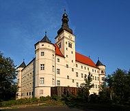 Photo en couleurs (18 août 2005) du château de Hartheim, en Bavière, centre d’euthanasie ouvert pendant la période nazie. La couleur beige très clair des deux façades visibles du château, à l’architecture de type Renaissance, contraste contre le ciel bleu, en arrière-plan, et la verdure au premier plan.